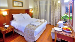 A hotel room with a bed, bedside lamps, a bedside table with a phone, a desk with a mirror, and a fruit bowl. - Perula Hotel & SPA (Istanbul)
