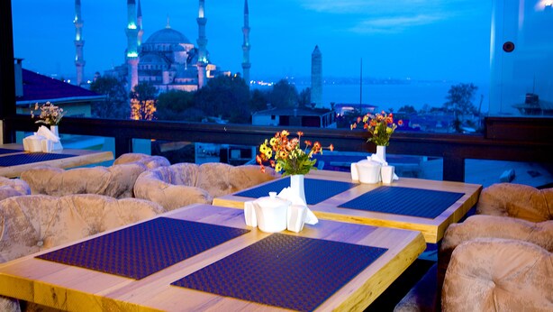 A restaurant with tables set for dining, a vase of flowers, and a view of a mosque with multiple minarets. - Perula Hotel & SPA (Istanbul)