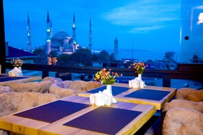 A restaurant with tables set for dining, a vase of flowers, and a view of a mosque with multiple minarets. - Perula Hotel & SPA (Istanbul)