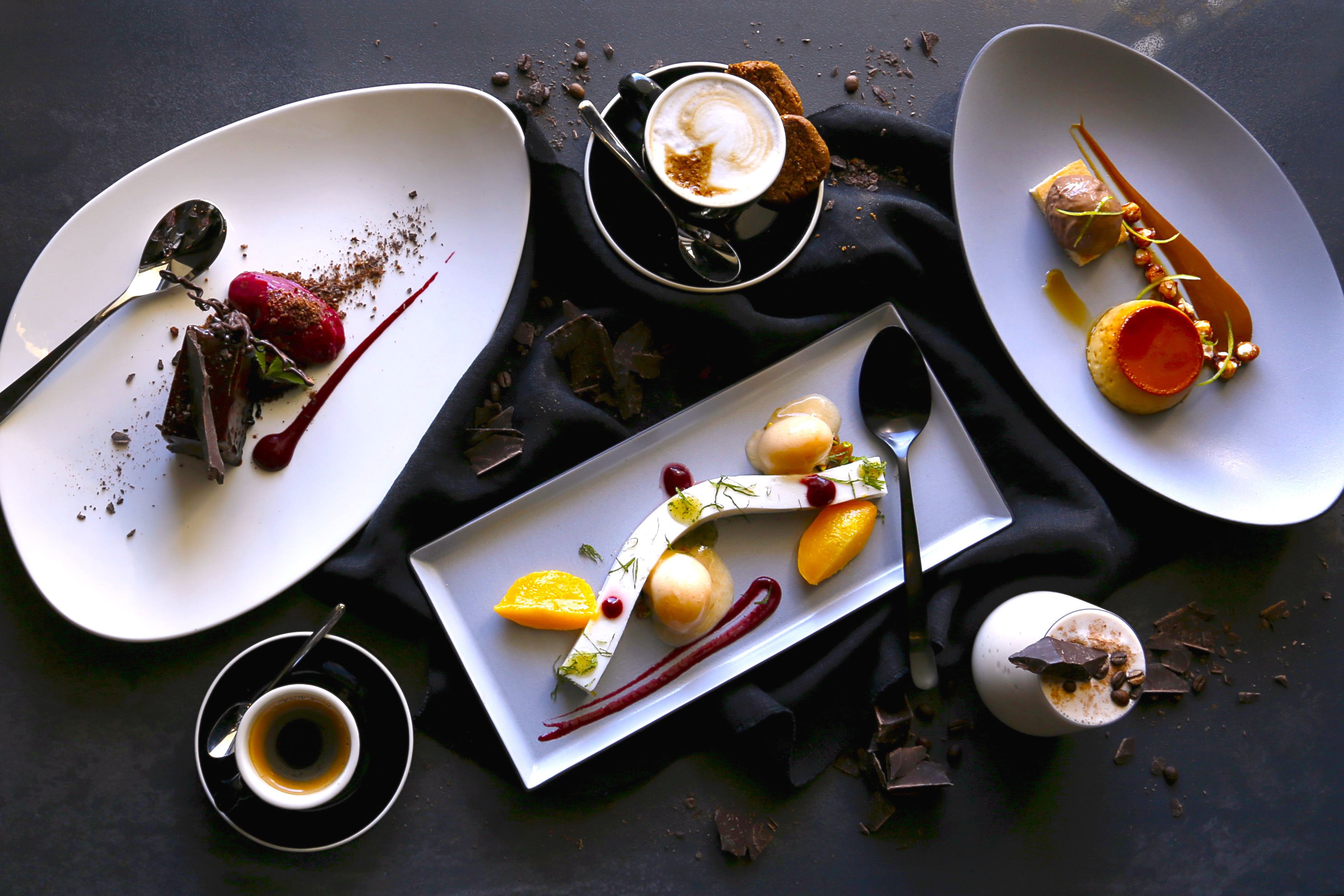 A dessert table with various plated desserts and a cup of coffee.