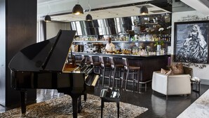 A modern bar area with a grand piano, bar stools, and a seating area with a white sofa and decorative pillows.
