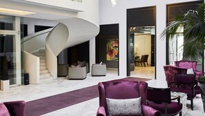 A modern lobby with a spiral staircase, plush seating, and large chandeliers.