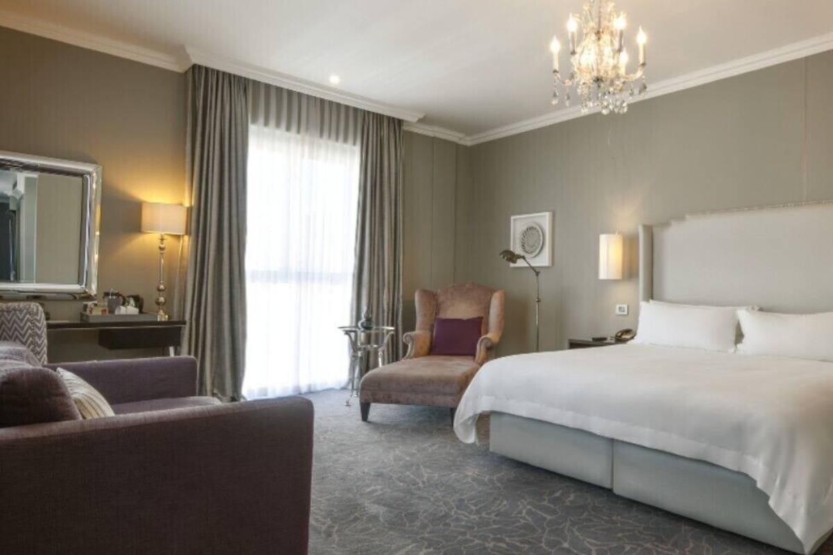 A hotel room with a large bed, a sitting area with a chair, a desk, and a chandelier.