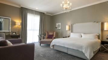 Une chambre d’hôtel avec un grand lit, un coin salon avec un fauteuil, un bureau et un lustre.