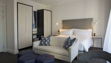 A modern hotel room with a bed, a sofa, a TV, and a wardrobe.