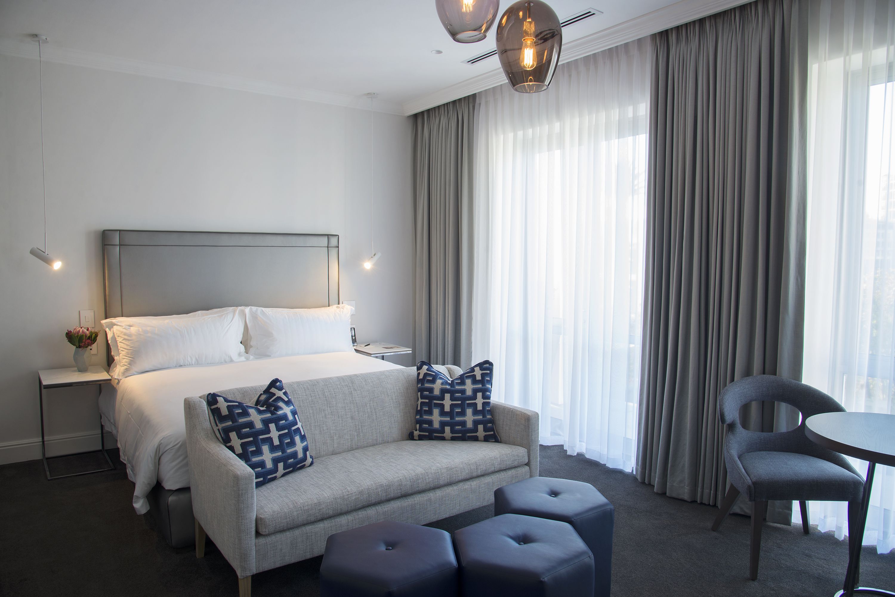 Une chambre d’hôtel moderne avec un lit soigneusement fait, un canapé agrémenté de coussins à motifs, une table à manger et une chaise.