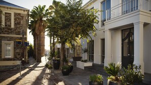 A cobblestone courtyard with potted plants, a palm tree, and a stone building with a signboard.
