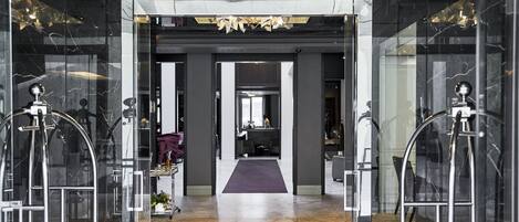 A modern lobby with marble floors, a central pathway, and glass doors leading to rooms.