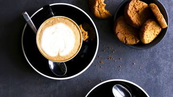 Two cups of coffee with latte art on a dark surface, accompanied by a bowl of cookies.