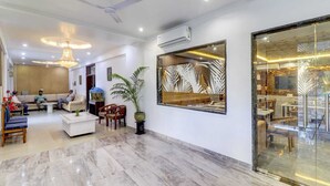 A spacious lobby with a marble floor, a large mirror, a ceiling fan, and a seating area with sofas and chairs. - Hotel Anand Villa (Agra)