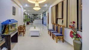A hotel lobby with a reception desk, a chandelier, a fish tank, and a row of chairs. - Hotel Anand Villa (Agra)