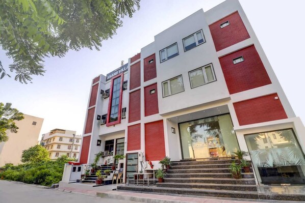 A modern hotel with a red and white facade, multiple balconies, and a staircase leading to the entrance.