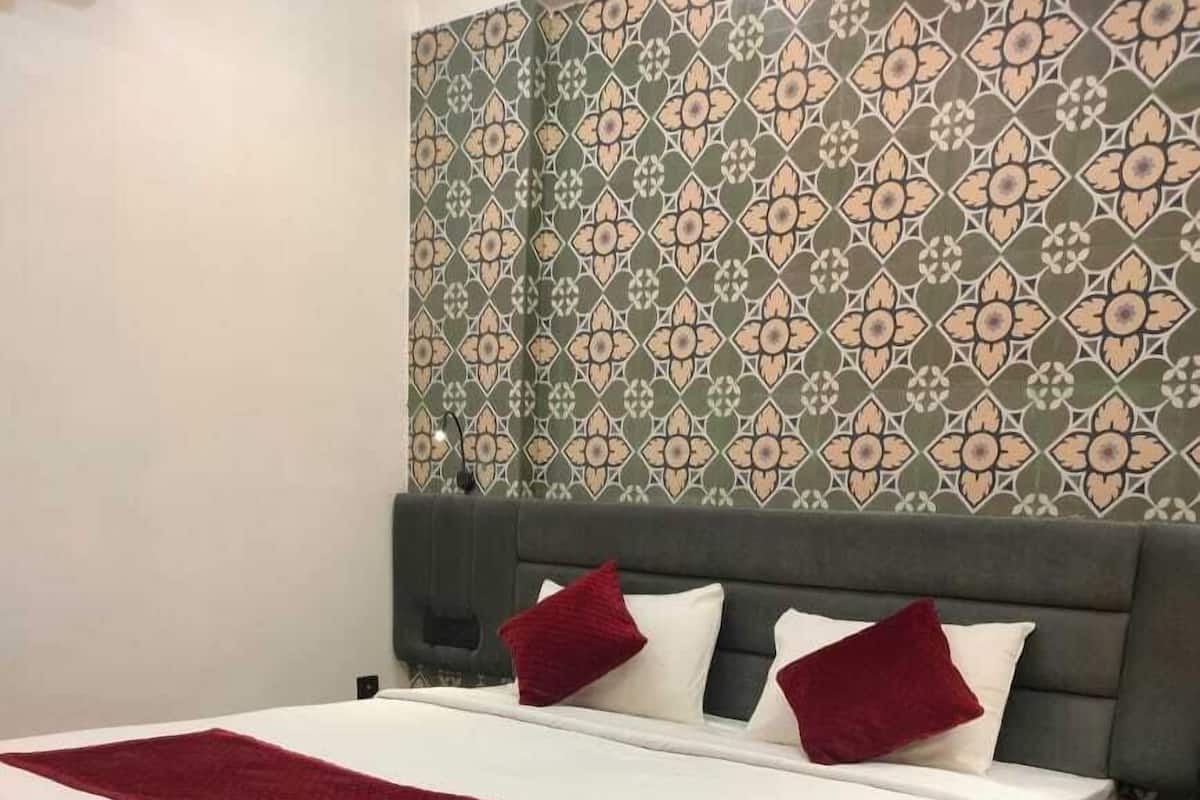 A neatly made bed with a white mattress and a red blanket, a dark wooden headboard, and a patterned wallpaper with a geometric design.
