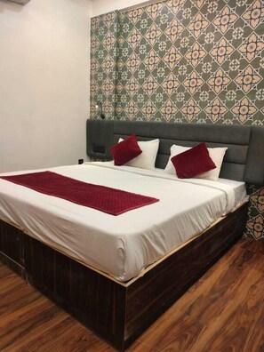 A neatly made bed with a white mattress and a red blanket, a dark wooden headboard, and a patterned wallpaper with a geometric design.