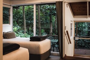A bedroom with a bed, a small table, and a balcony with a view of the forest.