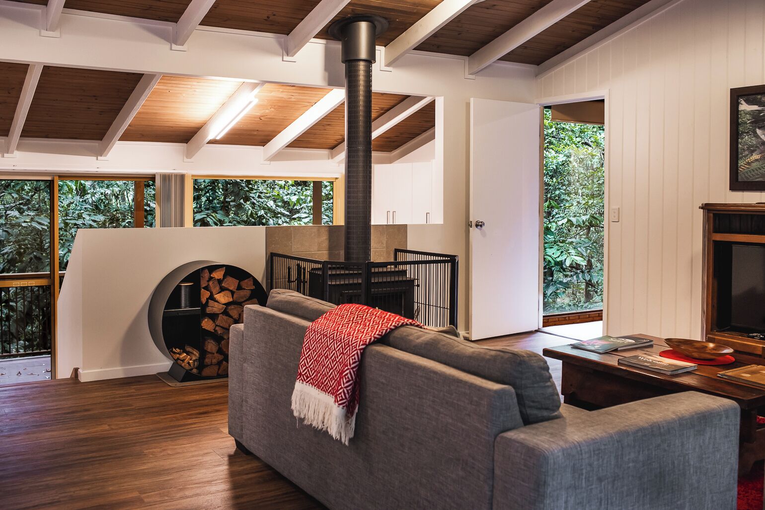 Uma sala de estar moderna com lareira, um sofá e uma janela grande com vista para o verde.