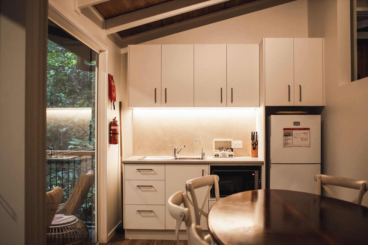 A modern kitchen with white cabinets, a built-in oven, and a dining area with a wooden table and chairs.