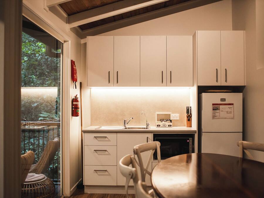 A modern kitchen with white cabinets, a built-in oven, and a dining area with a wooden table and chairs.