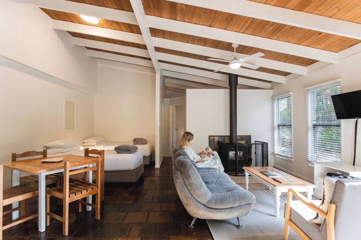 Ein gemütliches Wohnzimmer mit Kamin, Holzbalkendecke, einer Couch und einem Essbereich mit Tisch und Stühlen.