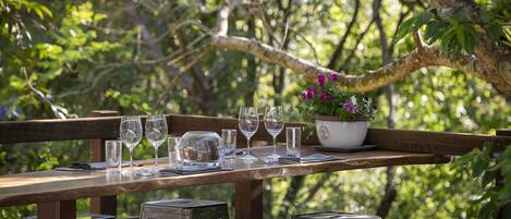 An outdoor dining area with a wooden table set for six, surrounded by metal stools.