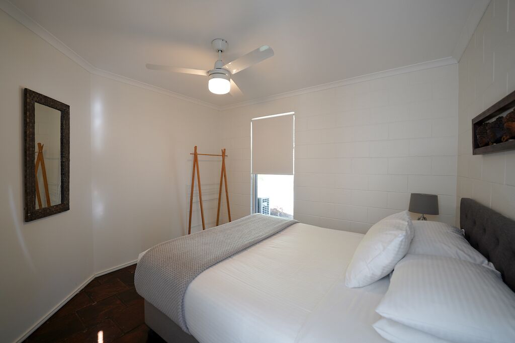 Une chambre à coucher avec un lit, un ventilateur de plafond, une fenêtre et un miroir au mur.