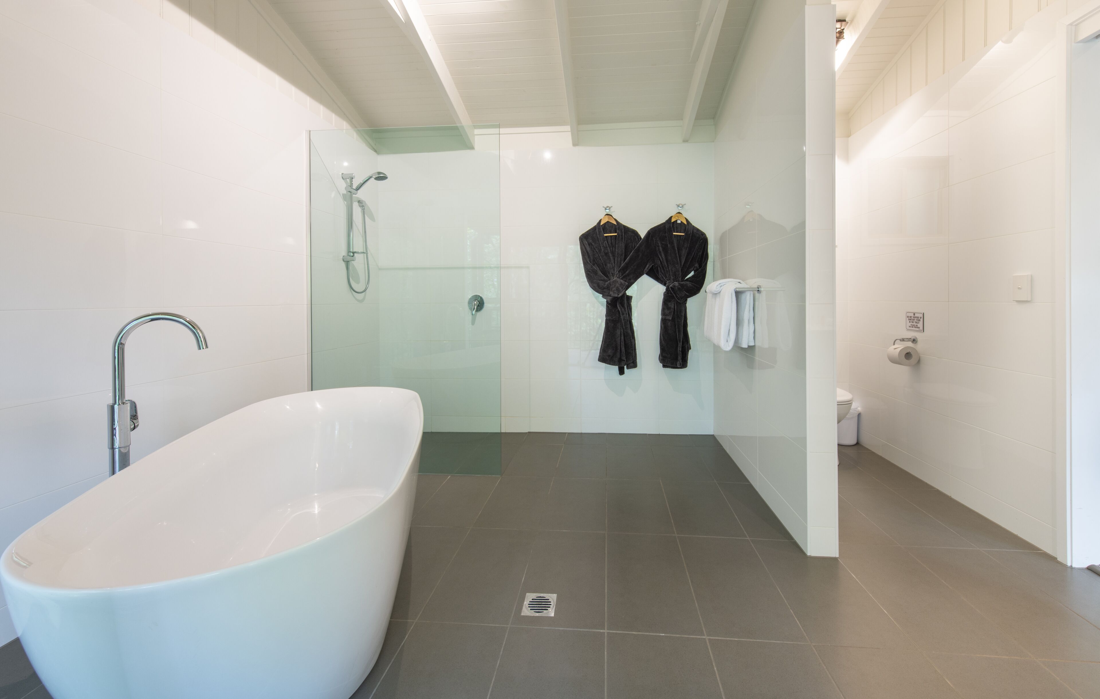Un baño moderno con una bañera independiente, cabina de ducha de vidrio y dos albornoces negros colgados en ganchos.