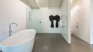 A modern bathroom with a freestanding bathtub, glass shower enclosure, and two black robes hanging on hooks.