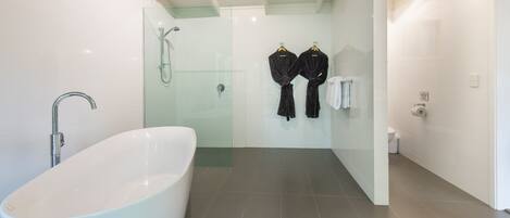 Un baño moderno con una bañera independiente, cabina de ducha de vidrio y dos albornoces negros colgados en ganchos.