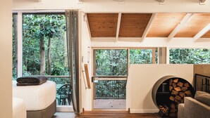 Una habitación acogedora con cama, una silla, chimenea y ventanas amplias con vistas al bosque.