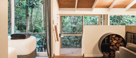 A cozy room with a bed, a chair, a fireplace, and large windows offering a view of the forest.