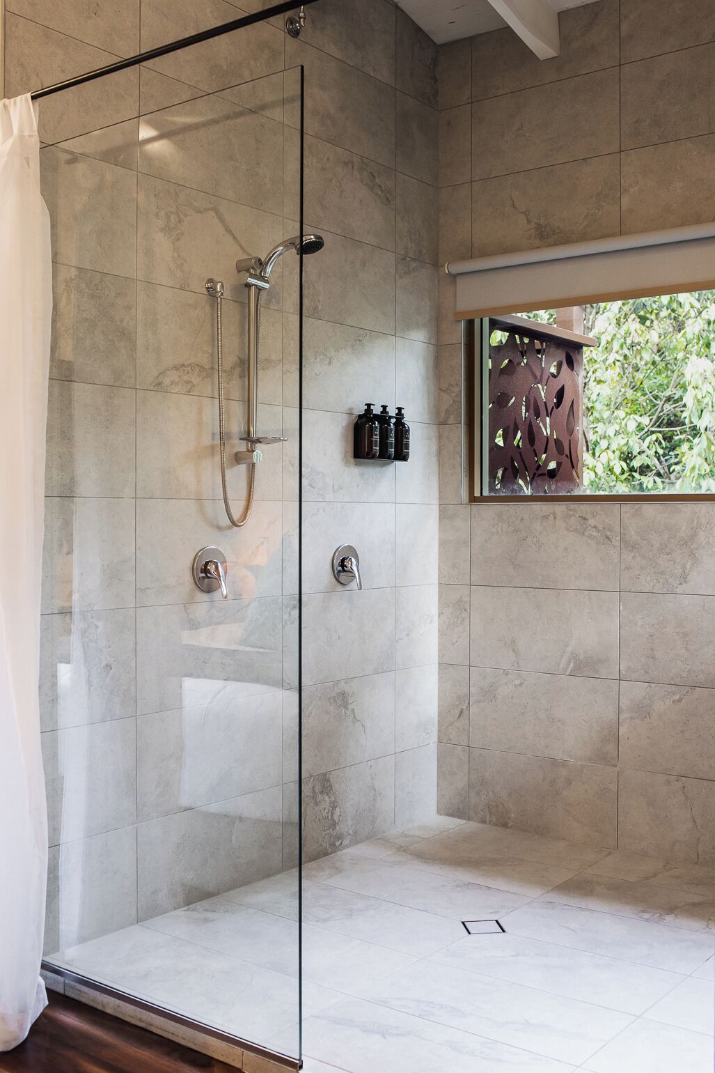 Une douche moderne avec une porte en verre, une fenêtre offrant une belle vue et une étagère pour les articles de toilette.