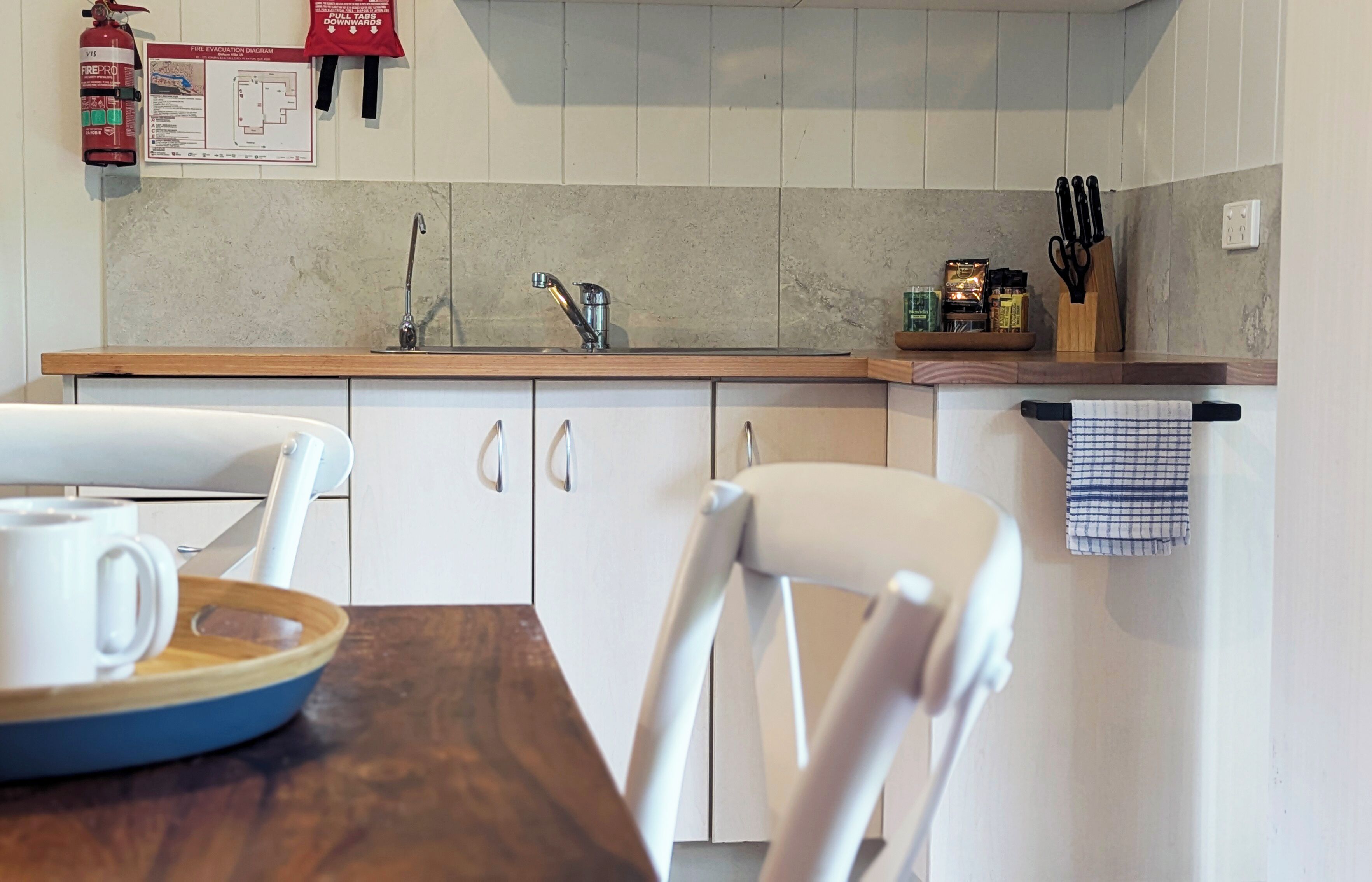 A kitchen with a wooden countertop, white cabinets, a sink, and a fire extinguisher.