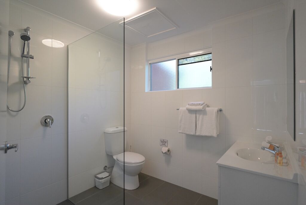 A modern bathroom with a glass shower enclosure, a toilet, a sink, and a small window.