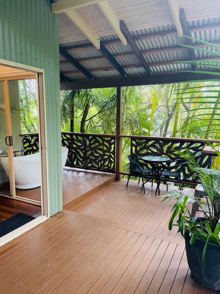A wooden deck with a glass door leading to a bathroom, surrounded by lush greenery.