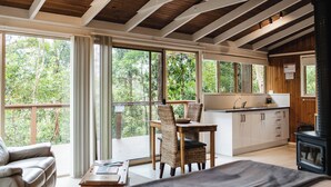 Una cabaña acogedora con comedor, cocina y un ventanal grande con vistas a un bosque.
