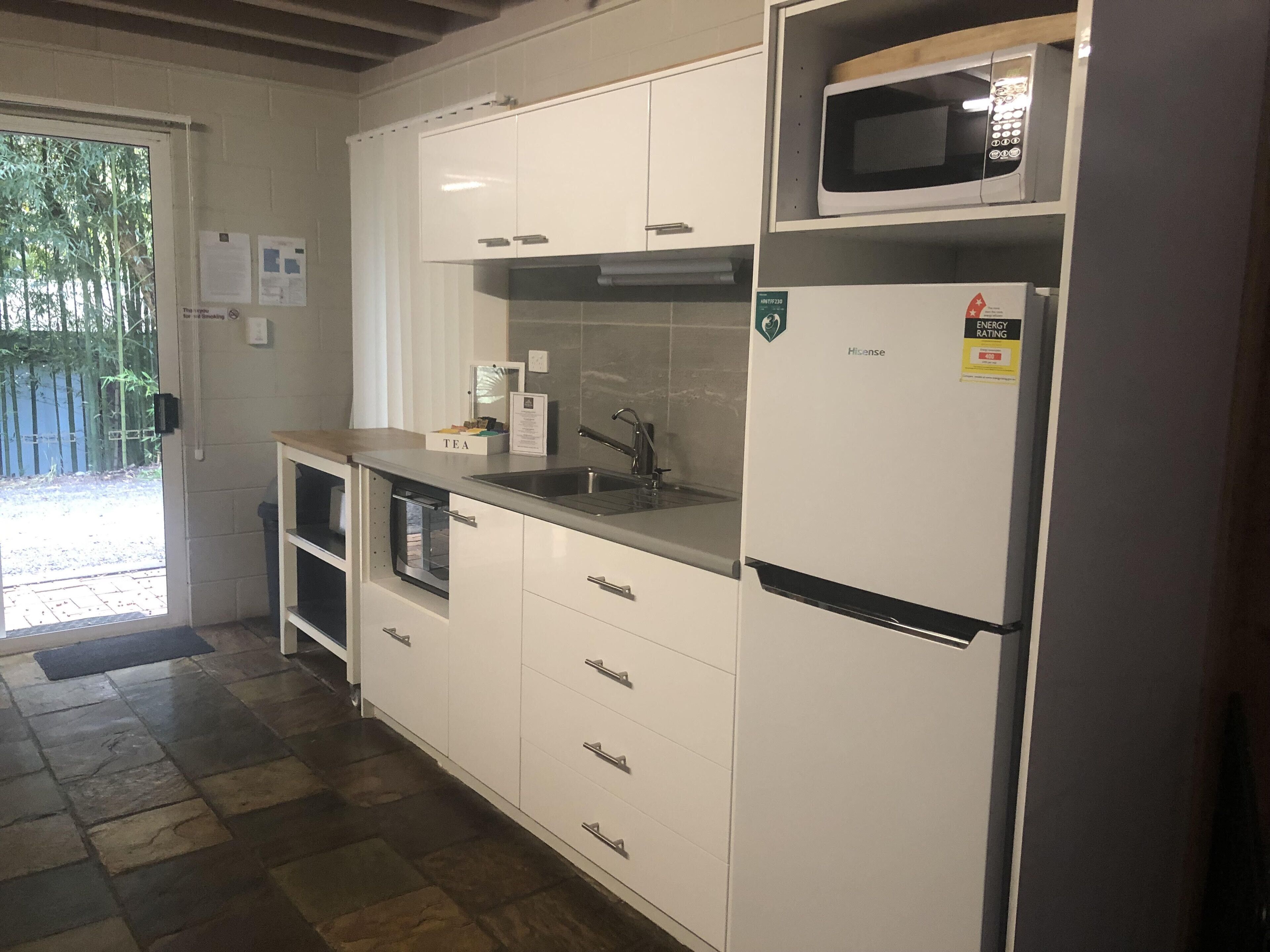 Een keuken met witte kastjes, een magnetron, een spoelbak en een koelkast.