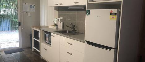 Een keuken met witte kastjes, een magnetron, een spoelbak en een koelkast.