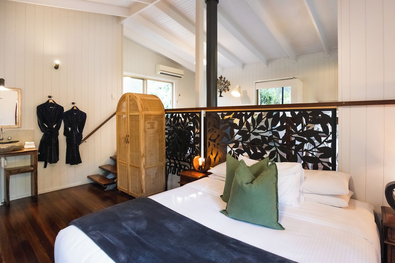 A bedroom with a bed, a wooden wardrobe, a mirror, and a staircase.
