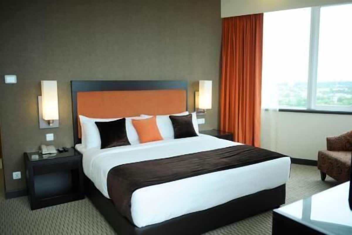 A hotel room with a large bed, a nightstand, a chair, and a window with curtains.