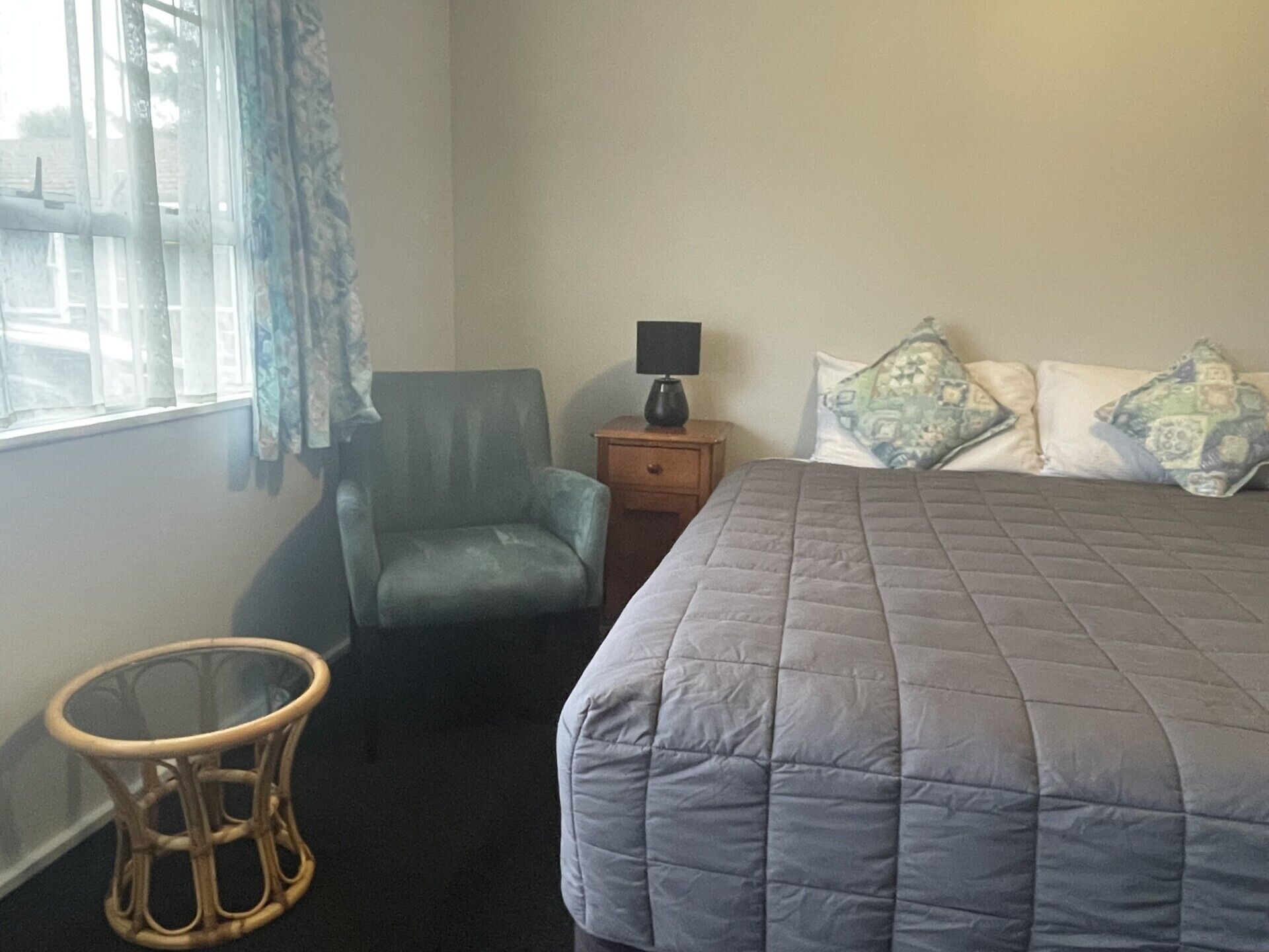 A bedroom with a bed, a chair, a nightstand, and a small table.