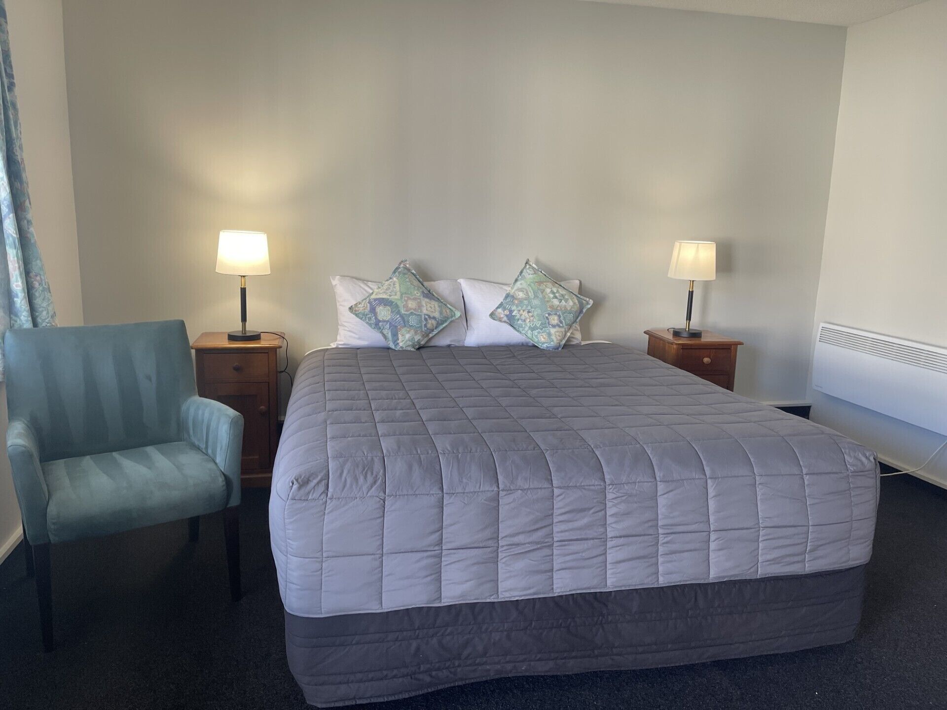 Une chambre d’hôtel avec un grand lit, deux tables de chevet avec des lampes, une chaise et un climatiseur fixé au mur.