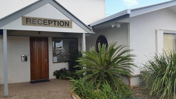 A reception area with a sign above the door, a window with office hours, and potted plants around the entrance.