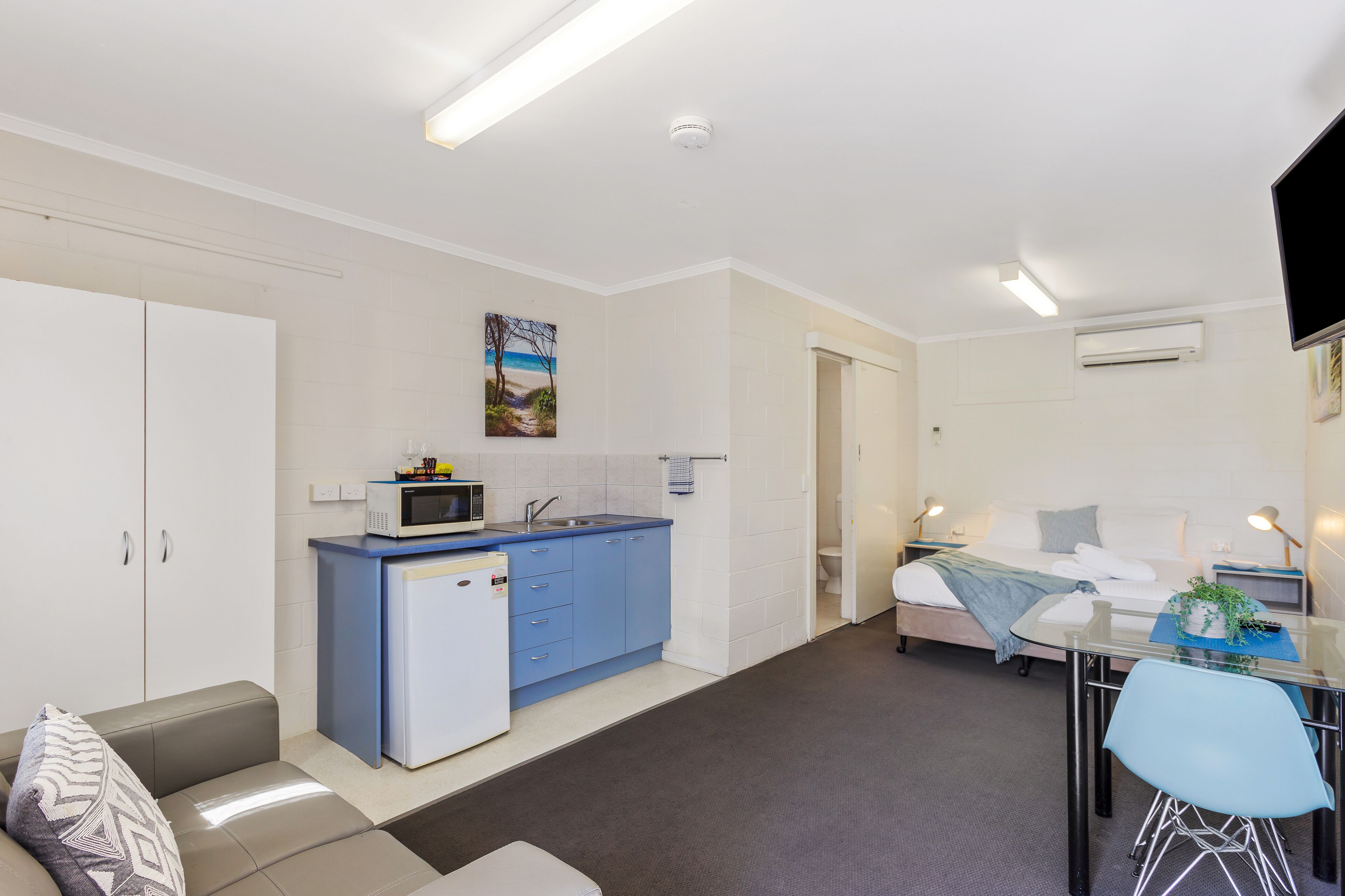 A compact living space with a kitchenette, a sofa, a dining table with chairs, and a bed.