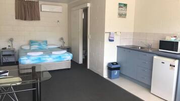 A compact hotel room with a bed, bedside table, lamp, and a small kitchenette with a microwave and refrigerator.