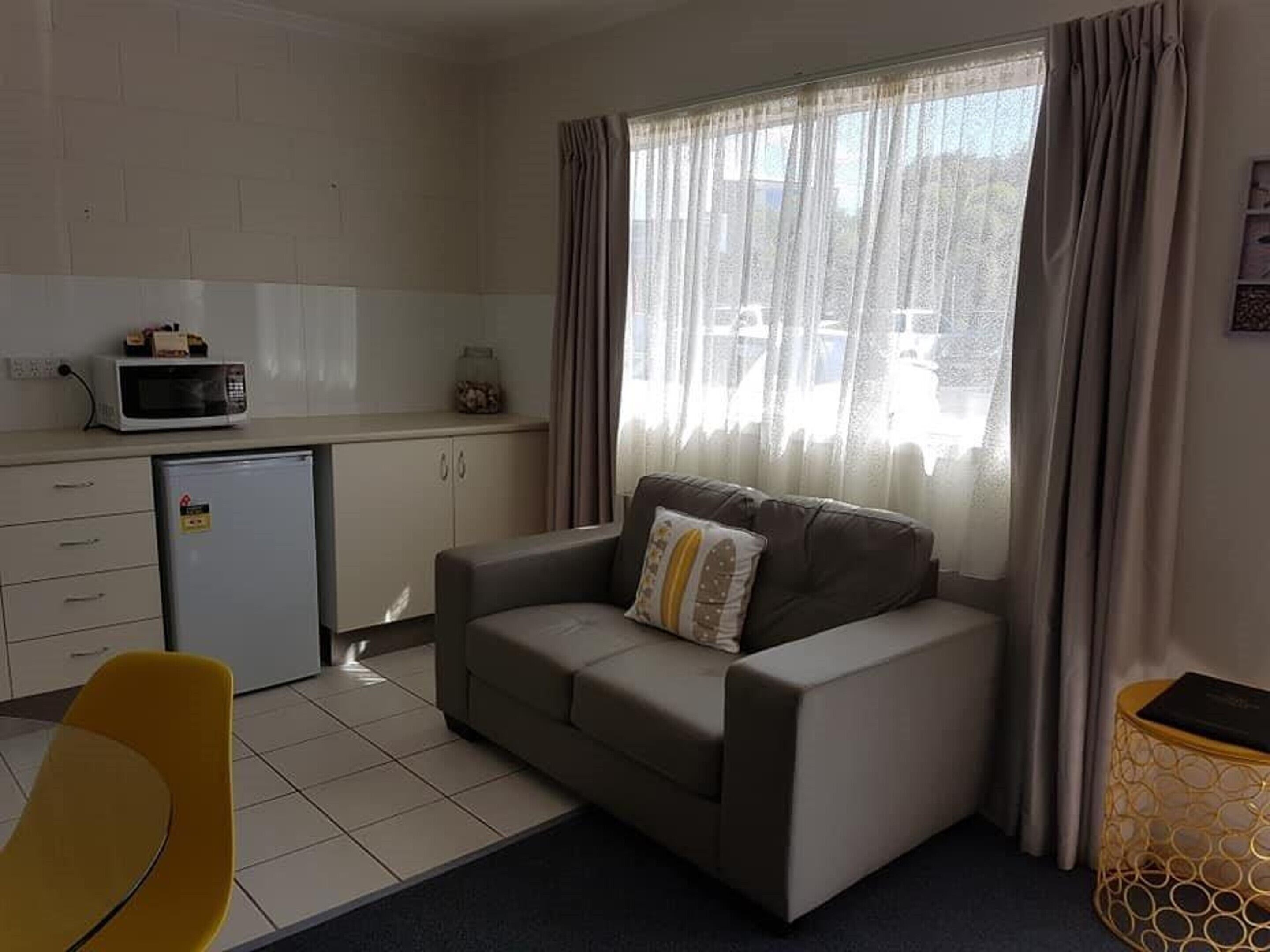 Espaço compacto com cozinha compacta, um sofá, uma pequena mesa de jantar e uma cadeira amarela.