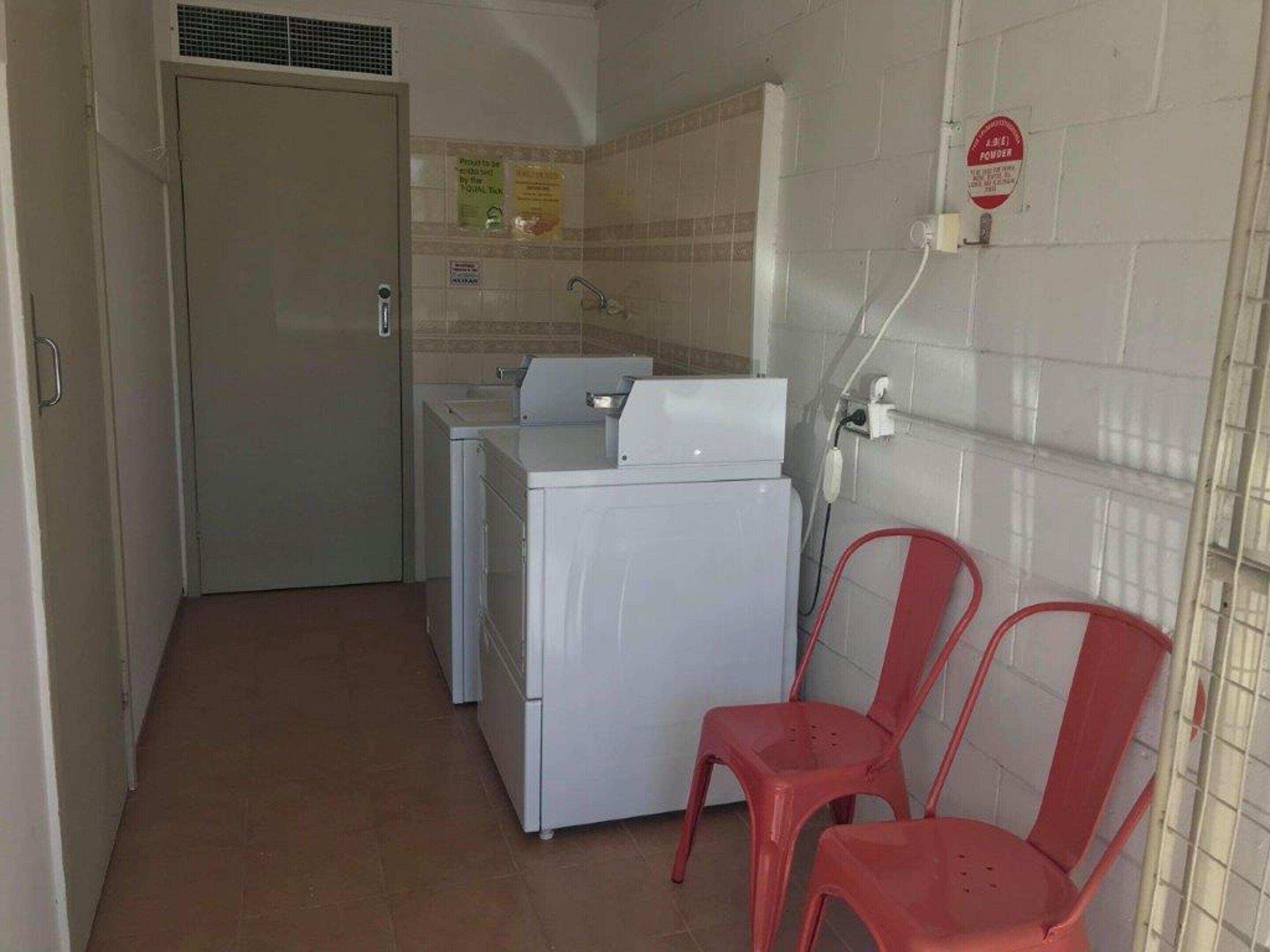A compact kitchen with a washing machine, a sink, and a red chair.
