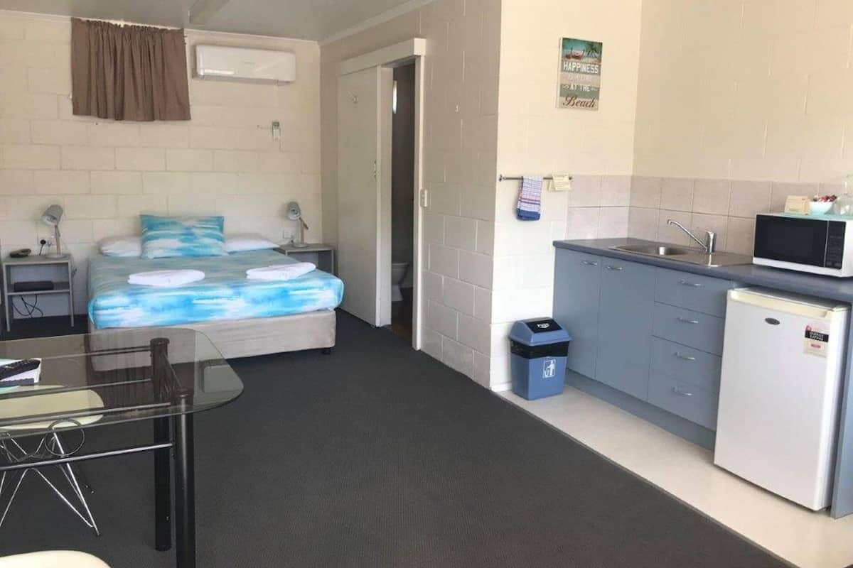 Habitación de hotel compacta con cama, escritorio pequeño, kitchenette y baño.