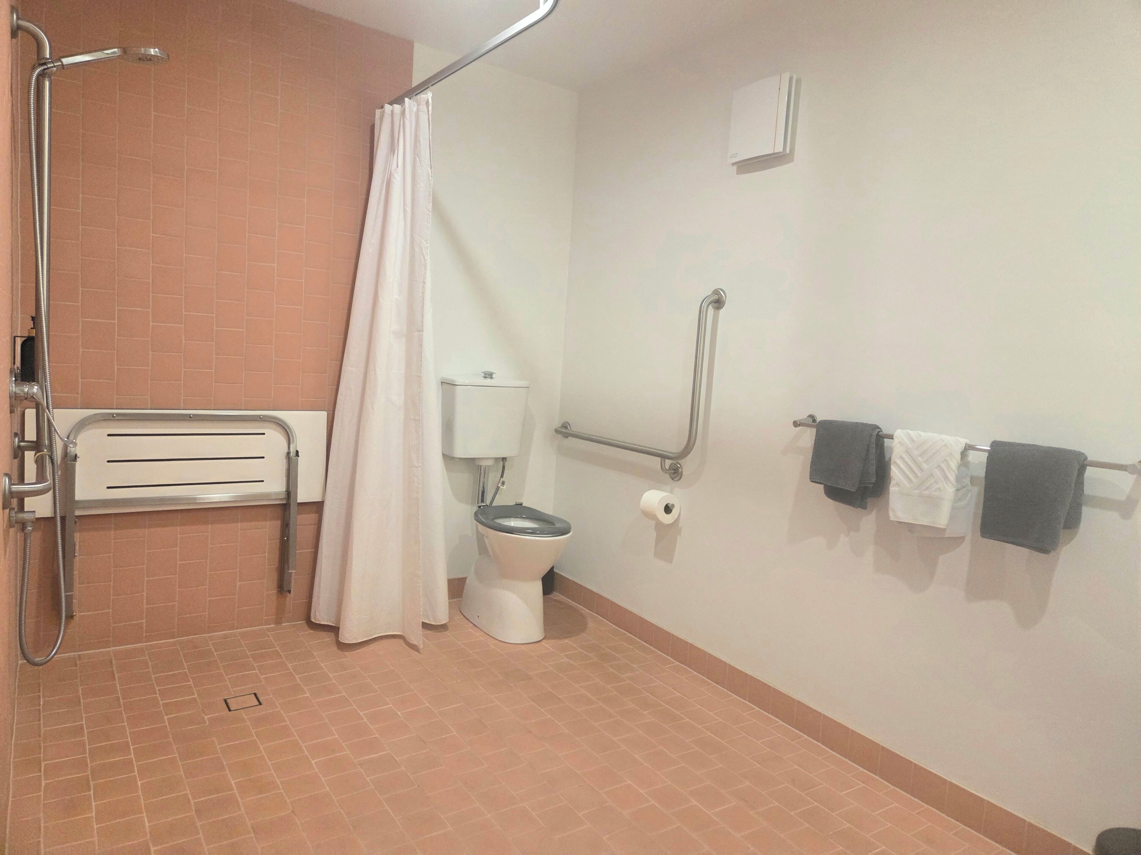 Une salle de bain équipée d’une douche, de toilettes, de barres d’appui et d’un porte-serviettes.