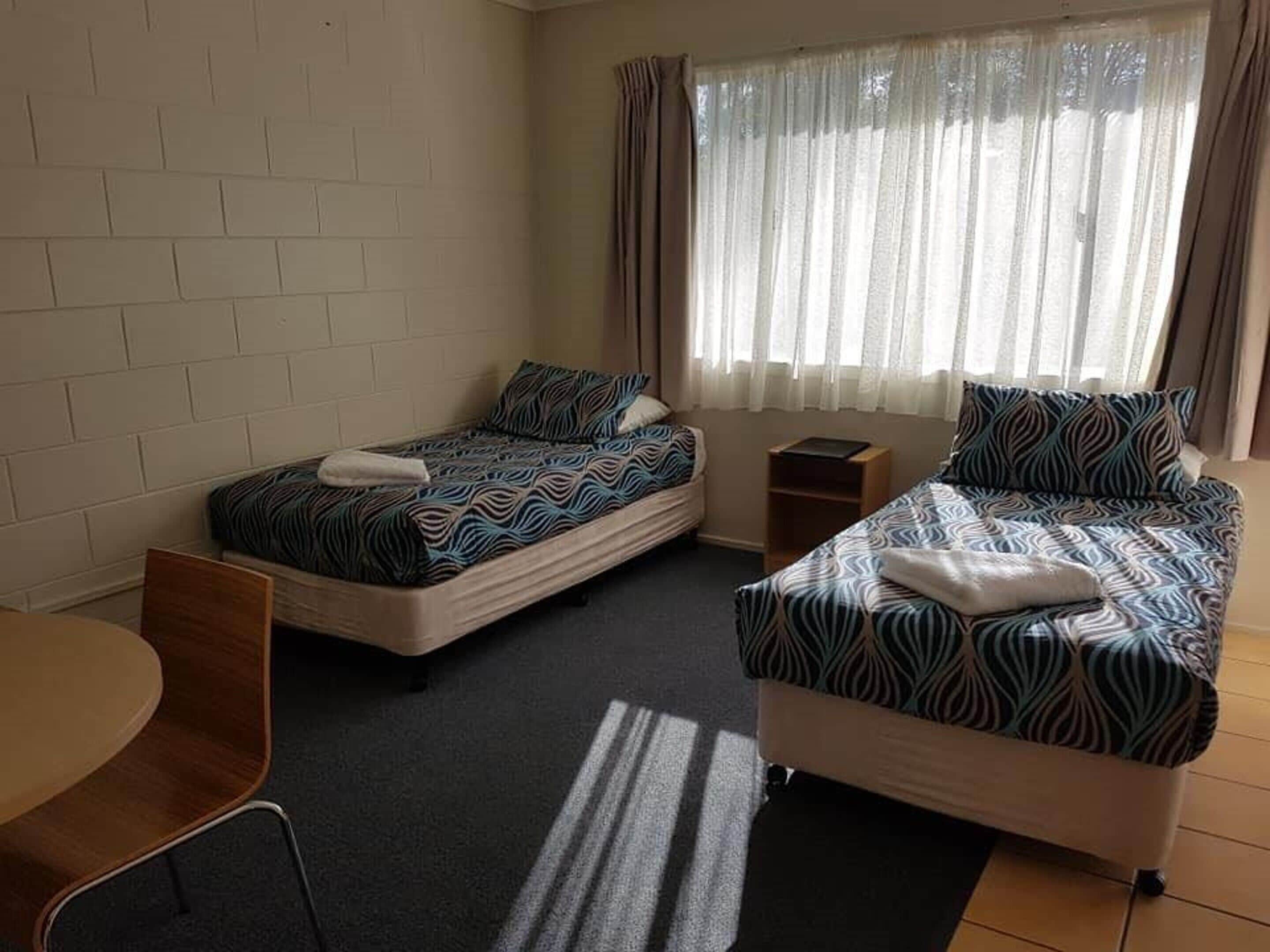 A hotel room with two single beds, a small table, and a chair.