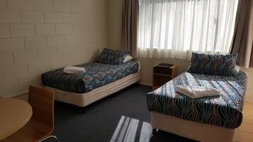 A hotel room with two single beds, a small table, and a chair.